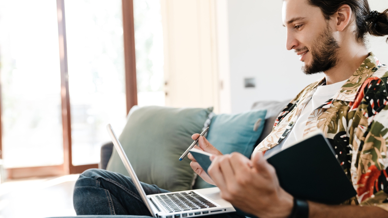 Freelancer radi na laptopu i beleži podatke u svesku.